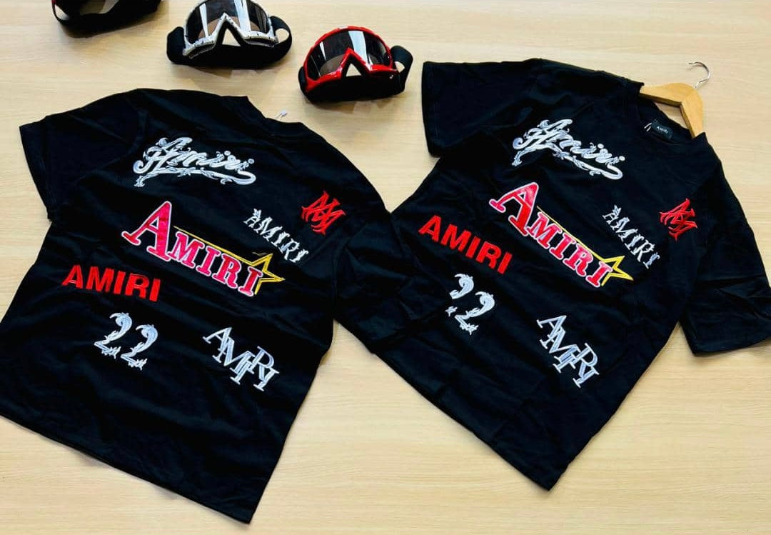 Black Amiri Multi-Logo T-Shirt with various bold, colorful Amiri brand logos and graphics printed across the back.