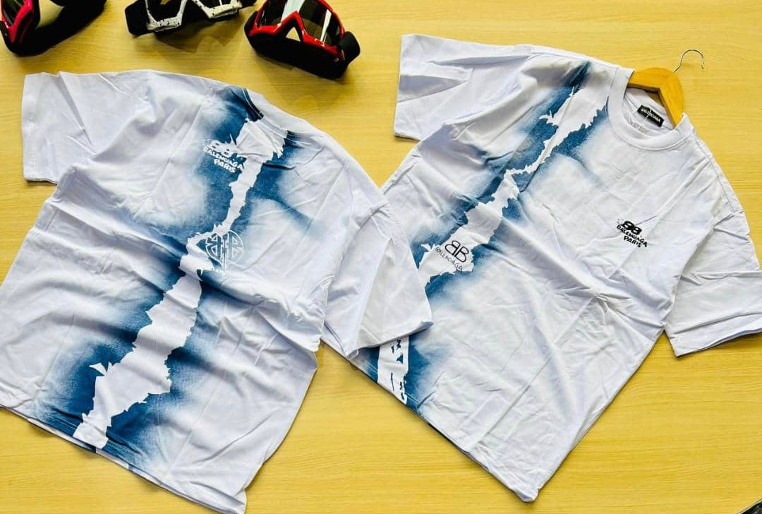 A stylish white t-shirt with a unique blue tie-dye pattern running vertically across the front and back, featuring subtle Balenciaga Paris branding