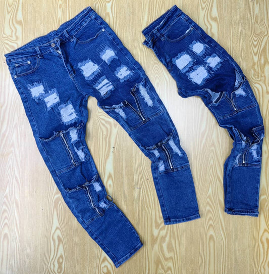 Blue distressed denim jeans with bold patchwork detailing, including rips, tears, and zipper accents